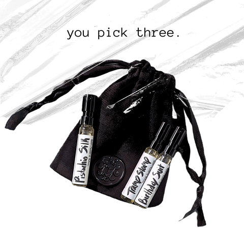 Black drawstring bag with three small bottles labeled 'pistachio silk', 'tramp stamp', and 'Birthday suit' on a white background.