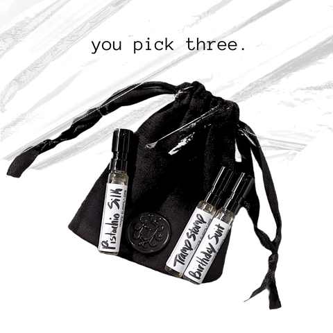 Black drawstring bag of fragrance samples with three small bottles labeled 'pistachio silk', 'tramp stamp', and 'Birthday suit' on a white background.