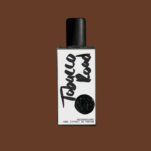 Tobacco Road Extrait de Parfum in a glass bottle with black cap and white label on a brown background. Niche Fragrances